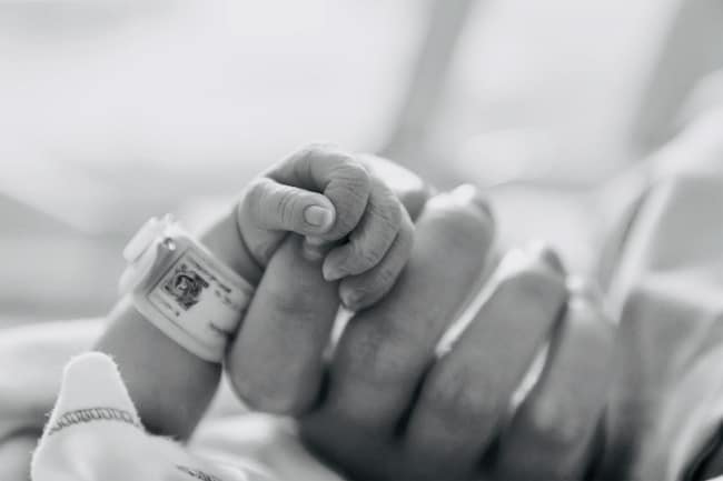 woman-holding-infants-hand-with-the-infant-wearing-a-hospital-band