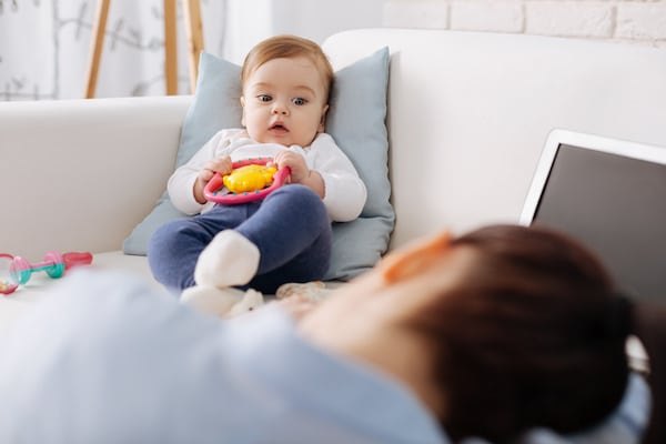 baby-staring-at-her-mother-who-has-her-head-on-a-desk-appearing-overwhelmed