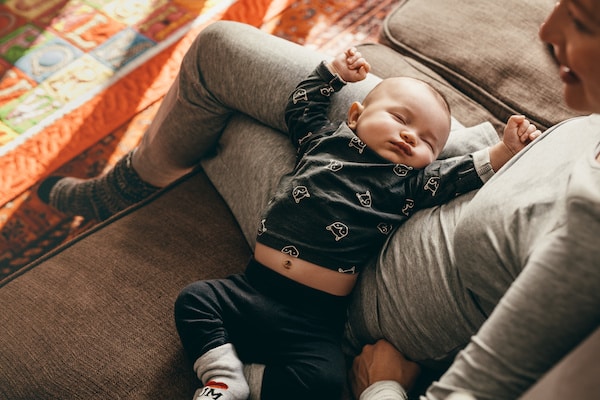 woman-sitting-on-the-couch-with-her-baby-sleeping-on-her-lap