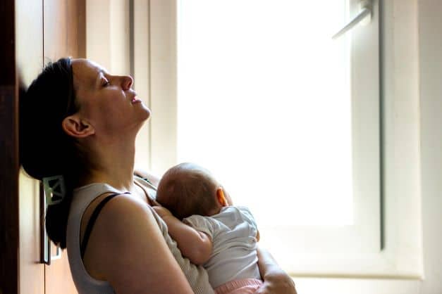 mother-leaning-against-a-wall-holding-her-baby-looking-overwhelmed