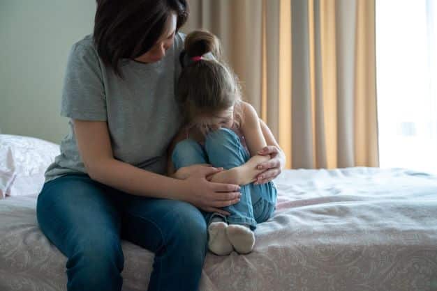 mother-protecting-sitting-on-the-bed-holding-her-daughter-protecting-her-from-a-violent-world