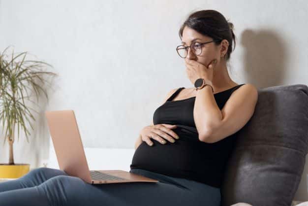 pregnant-woman-sitting-on-the-couch-looking-at-her-computer-feeling-anxious