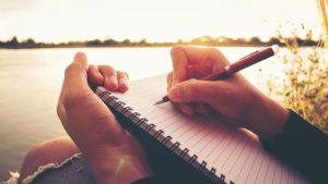 person-sitting-by-the-water-writing-in-a-journal-about-their-pregnancy-loss