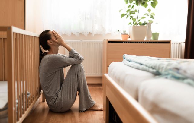 woman-sitting-on-the-floor-beside-a-crib-with-her-hands-over-her-face-struggling-with-postpartum