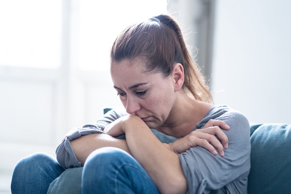 woman-sitting-on-the-couch-holding-her-knees-crying-due-to-grief-from-pregnancy-loss