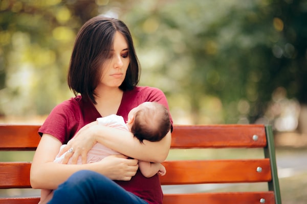 woman-sitting-on-a-park-bench-looking-at-her-baby-in-her-arms-with-disdain-after-birth-trauma